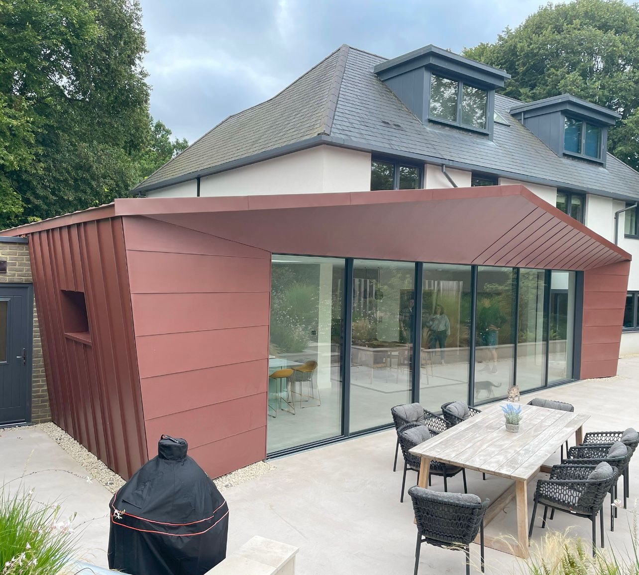 Matt red standing seam rear extension with full height glazing and a paved terrace